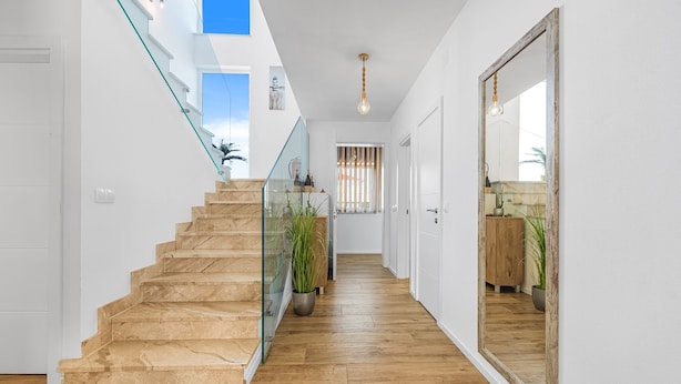 Un intérieur moderne avec un escalier en bois, des rampes en verre et un grand miroir.