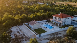Vue aérienne d’une maison moderne dotée d’une piscine, entourée de verdure et située dans un paysage vallonné.