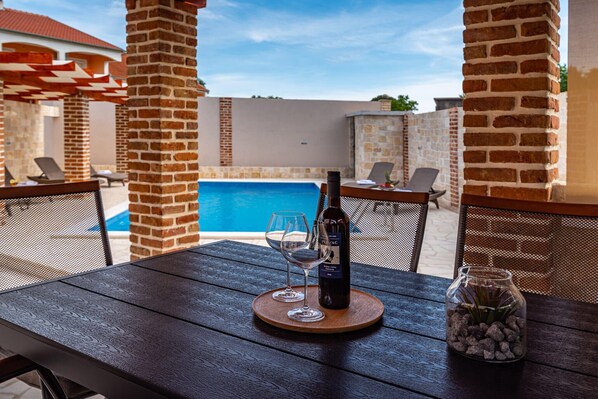 A poolside table with a bottle of wine, two glasses, and a decorative jar.