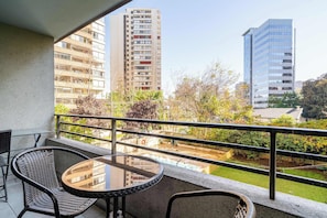 Ein Balkon mit Tisch und Stühlen, der auf einen Innenhof mit Grünflächen und Gebäuden blickt.