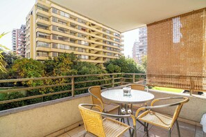 En balkon med fletstole og et bord, med udsigt over en by med høje bygninger og grønt.