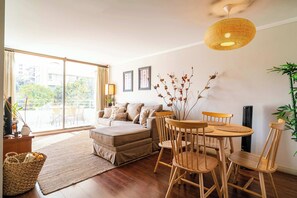 A living room with a sofa, a dining table with chairs, a large window, and a hanging light fixture.