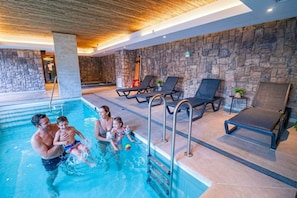 Ein Hallenbad mit Steinwänden, Liegestühlen und einer Holzbalkendecke.