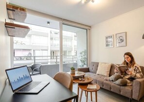 Un salon moderne avec un ordinateur portable posé sur une table, un canapé et une personne qui lit un livre.