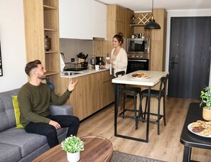 A modern kitchen with wooden cabinets, a dining area with a table and chairs, and a living room with a sofa and a coffee table. - HOM |  1D1B, Calefactor eléctrico WiFi Lavandería (Santiago)