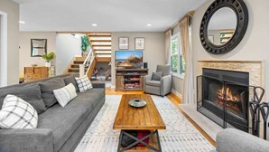 Una sala de estar con sofá, mesa de centro, chimenea y una escalera que sube a otro nivel.