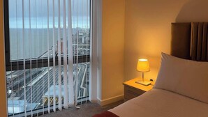 Ett hotellrum med en säng, ett nattduksbord med en lampa och utsikt över en bro och stadens silhuett genom fönstret.