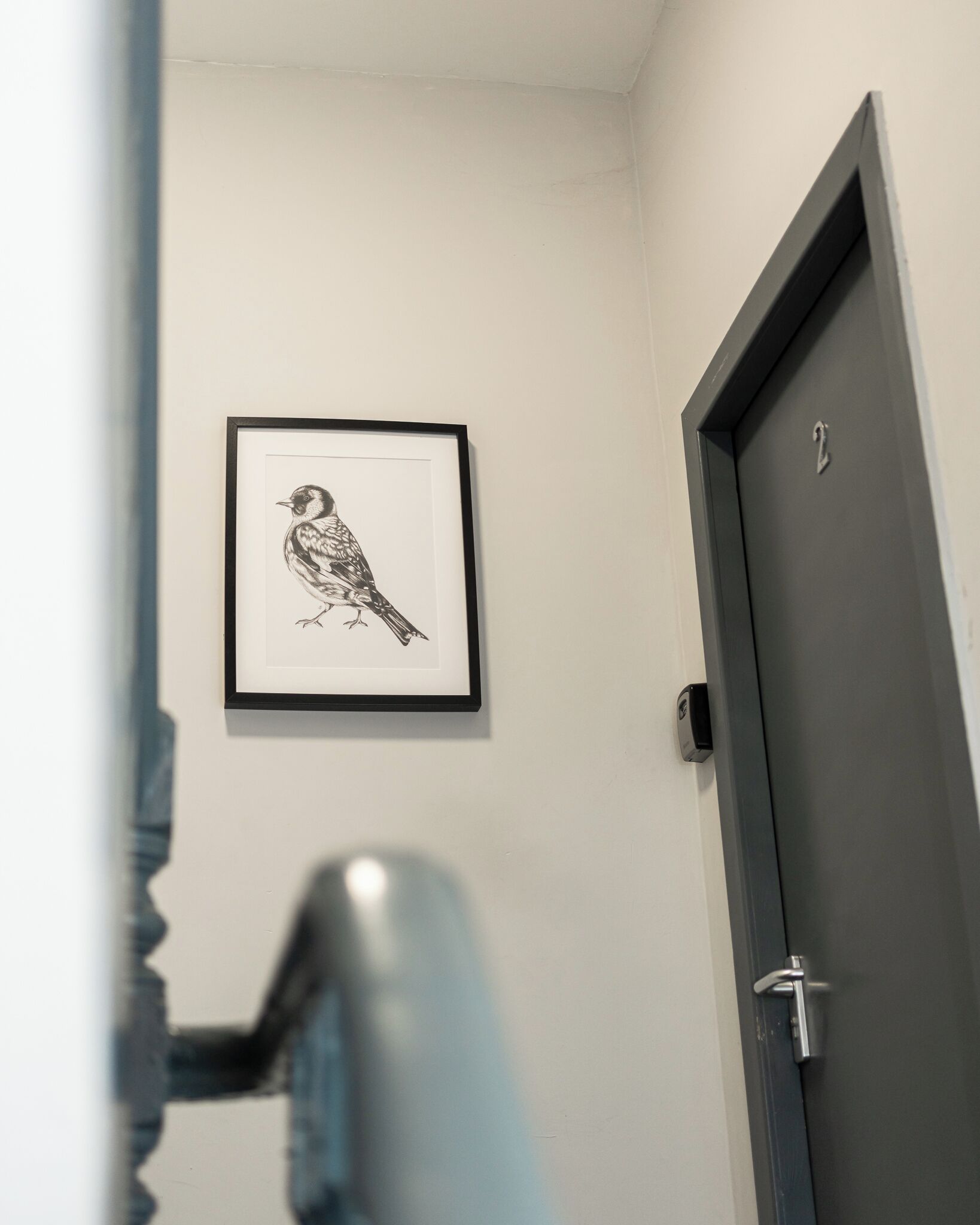 A framed black and white bird artwork on a white wall, a door with a number '2' sign, and a door handle.
