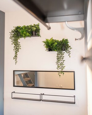 A bathroom with a large mirror, two black floating shelves, and three hanging planters with green foliage.