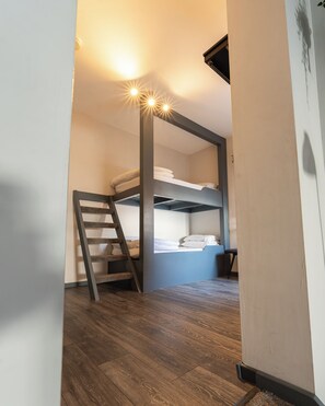 A bunk bed with a ladder, a small table, and a chair in a room with wooden flooring and a white wall.
