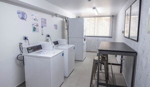 A laundry facility with industrial washing machines, a table, and a window.