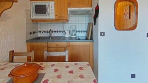 A compact kitchen with wooden cabinets, a microwave, a coffee maker, and a small window. - Ground floor, view village, balcony, tv, 22m², Le Grand Bornand (Le Grand-Bornand)