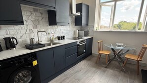 A modern kitchen with dark cabinets, a built-in oven, and a washing machine. - Desborough Apartment Retreat (Kettering)