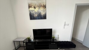 A modern living room with a flat-screen TV, a black entertainment unit, a grey sofa, and a painting on the wall. - Desborough Apartment Retreat (Kettering)