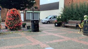 A paved courtyard with a brick pattern, a car parked in the background, and a bench with potted plants. - Desborough Apartment Retreat (Kettering)