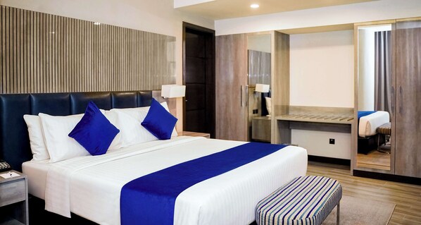Een hotelkamer met een groot bed, nachtkastje, spiegel en kledingkast.
