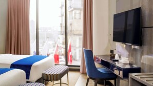 Une chambre d’hôtel équipée d’un lit, d’un bureau, d’une chaise, d’une télévision et d’une fenêtre avec des rideaux.
