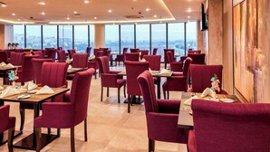 Un restaurant avec des chaises et des tables aux assises rouges, de grandes fenêtres donnant sur la ville et un décor intérieur moderne.