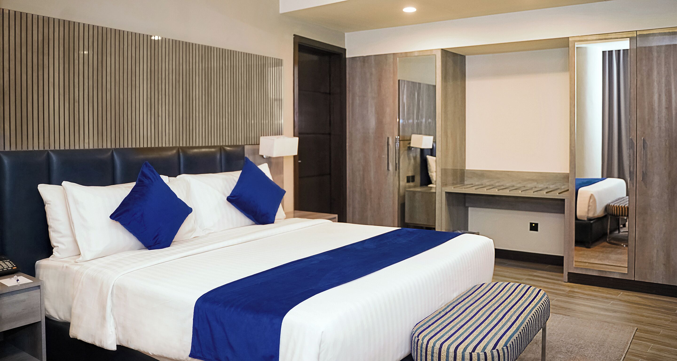 Hotelkamer met een groot bed, nachtkastje, bureau, spiegel en een badkamer door een open deur zichtbaar.