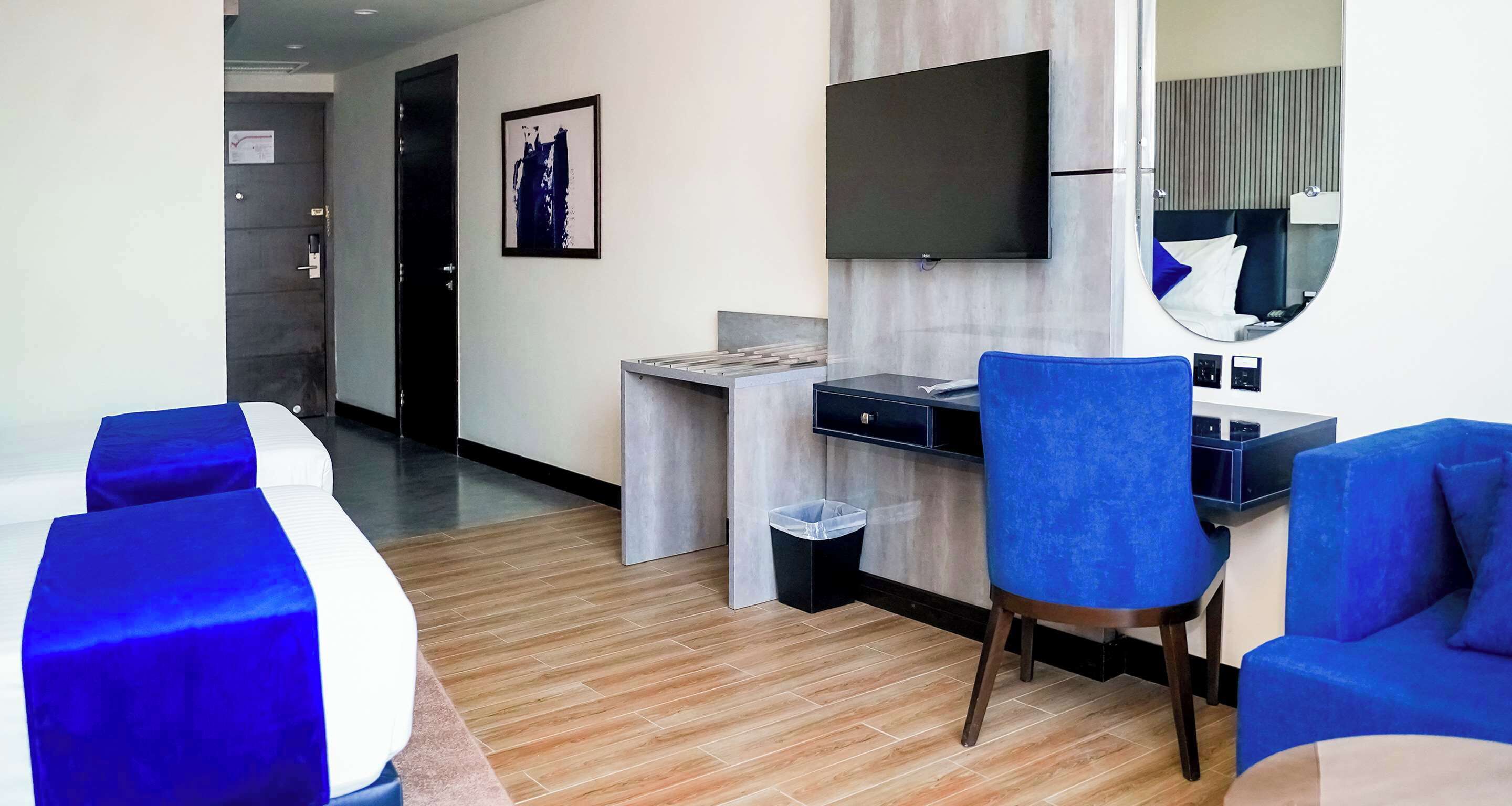 A hotel room with a bed, a desk, a chair, a TV, and a mirror.