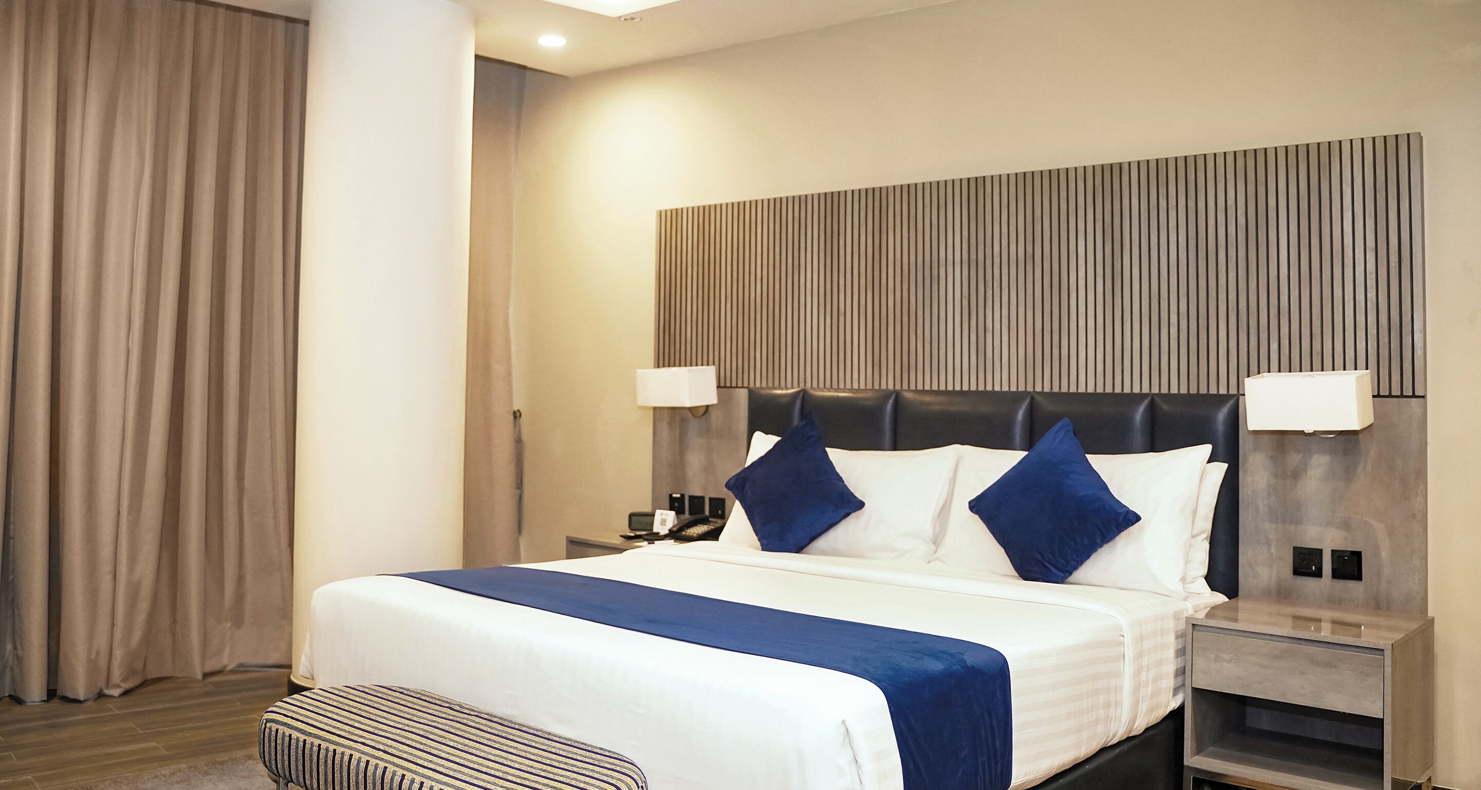 Una habitación de hotel con cama, mesitas de noche, lámpara y cortina.