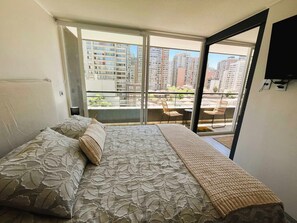 Relax on the large bed with a view of the city from the balcony, featuring a table and chairs.