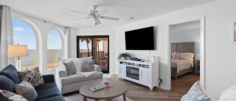Un salón moderno con sofá, sillón y mesa de centro, un televisor de pantalla plana montado en la pared y vistas al océano a través de grandes ventanales.