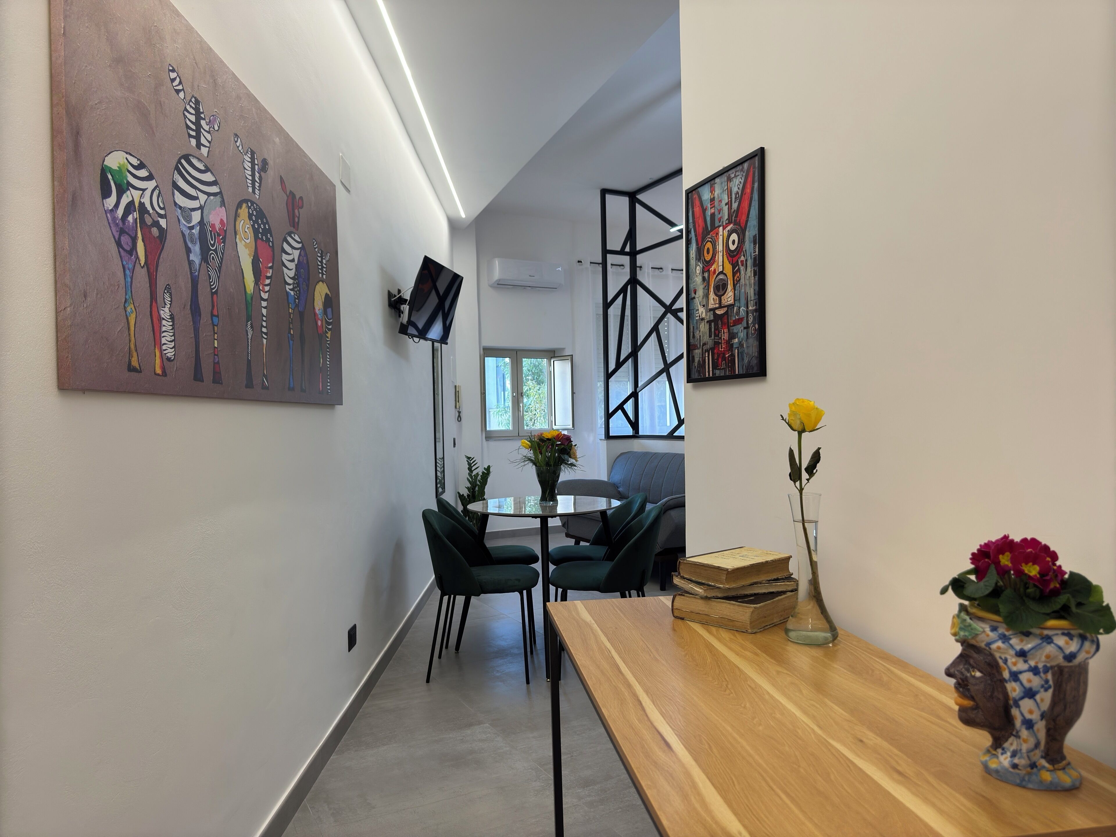 Un interno moderno con zona pranzo, opere d'arte alle pareti e un tavolo in legno con un vaso di fiori.