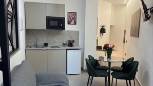 A modern kitchen with a built-in microwave, a coffee machine, and a refrigerator. There is a dining area with a table and chairs, and a sofa in the foreground. - La Dimora del Centro - Agrigento Complete apartment in the heart of the City (Agrigento)
