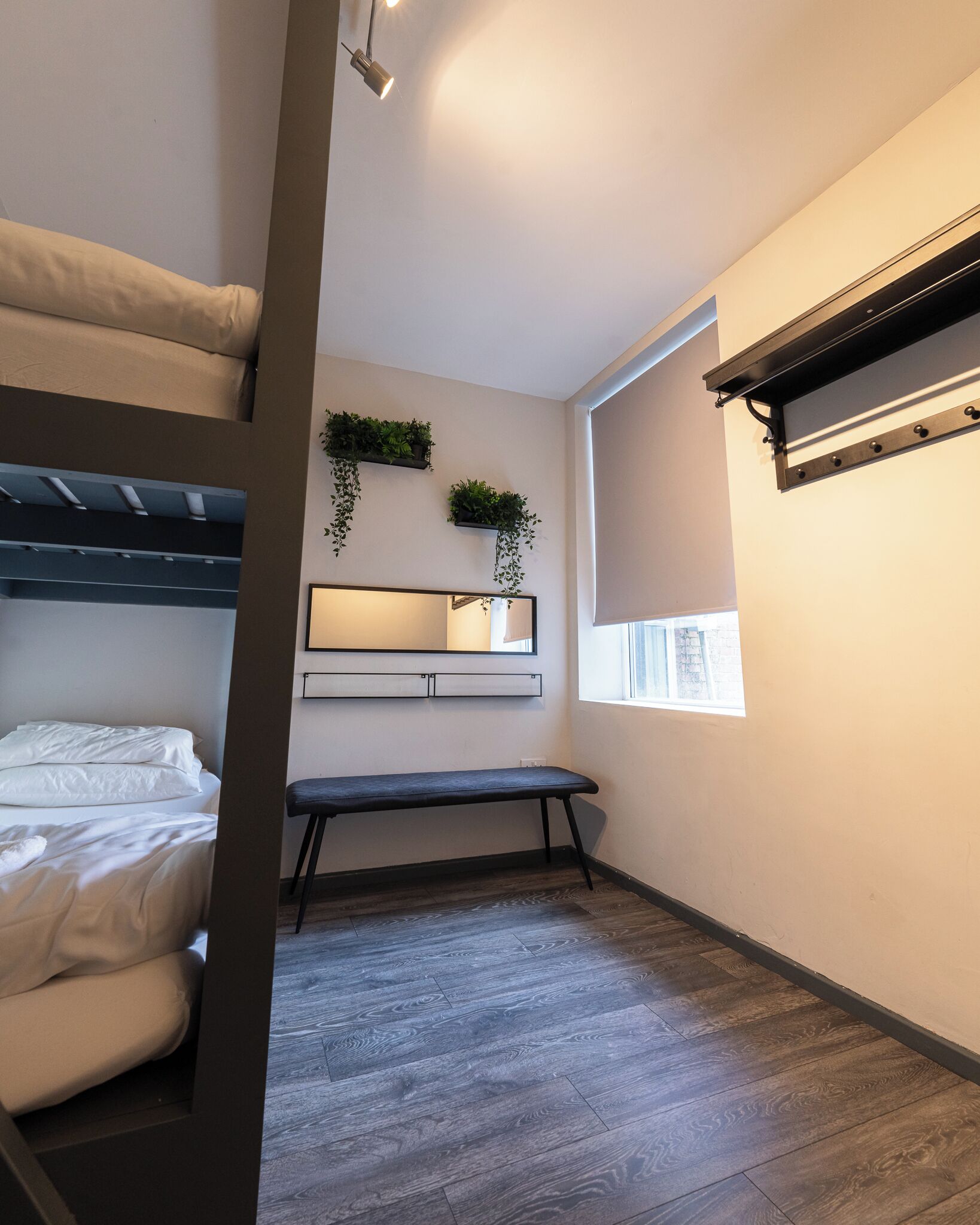 Une pièce de taille modeste, comprenant un lit superposé, un petit bureau avec un miroir et un banc.