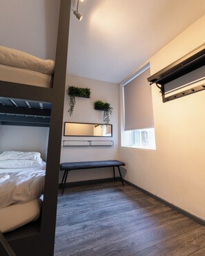 Une pièce de taille modeste, comprenant un lit superposé, un petit bureau avec un miroir et un banc.