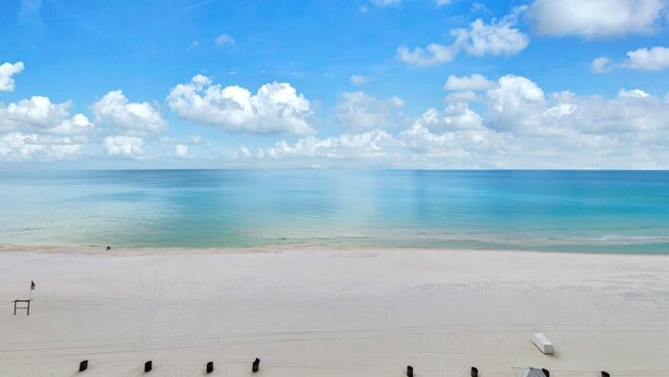 A beach with a clear sky, calm sea, and a few chairs on the sand. - Majestic Beach Towers 2-801 (Panama City Beach)