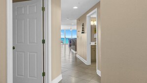 A hallway with a white door, beige walls, and a view of the ocean through large windows. - Majestic Beach Towers 2-801 (Panama City Beach)