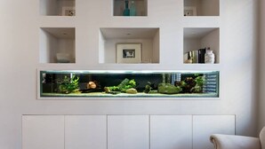 A modern living room with a large aquarium on the wall, white cabinetry below, and a beige sofa. - Spectacular 4 Bed House, Pimlico (London)
