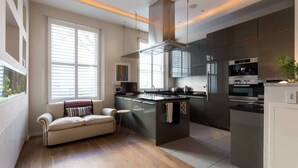 A modern kitchen with a central island, built-in appliances, and a cozy seating area with a sofa and a small table. - Spectacular 4 Bed House, Pimlico (London)