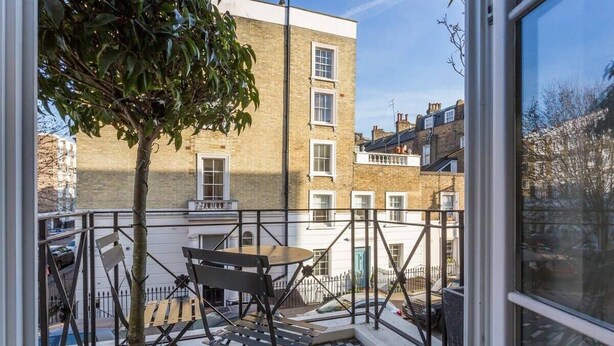 A balcony with a table and chairs, a tree, and a view of neighboring buildings. - Spectacular 4 Bed House, Pimlico (London)