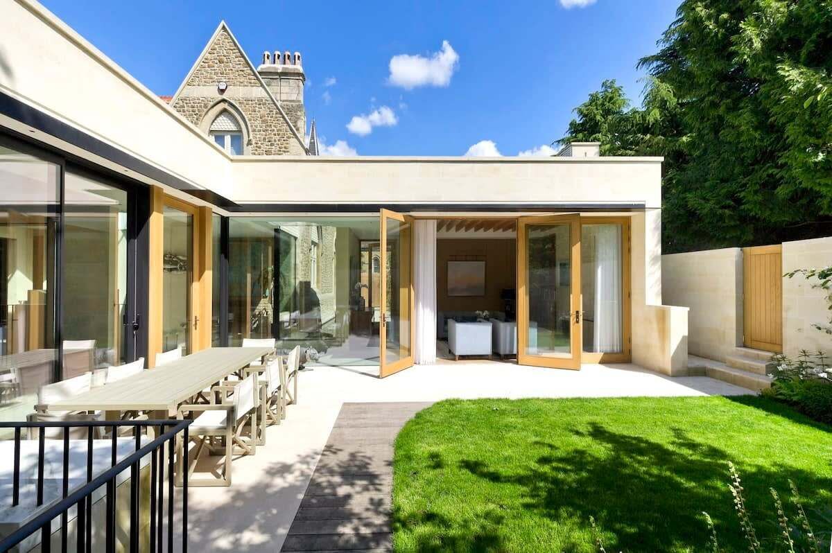 A modern house with a patio, a dining area, and a view of a stone building.