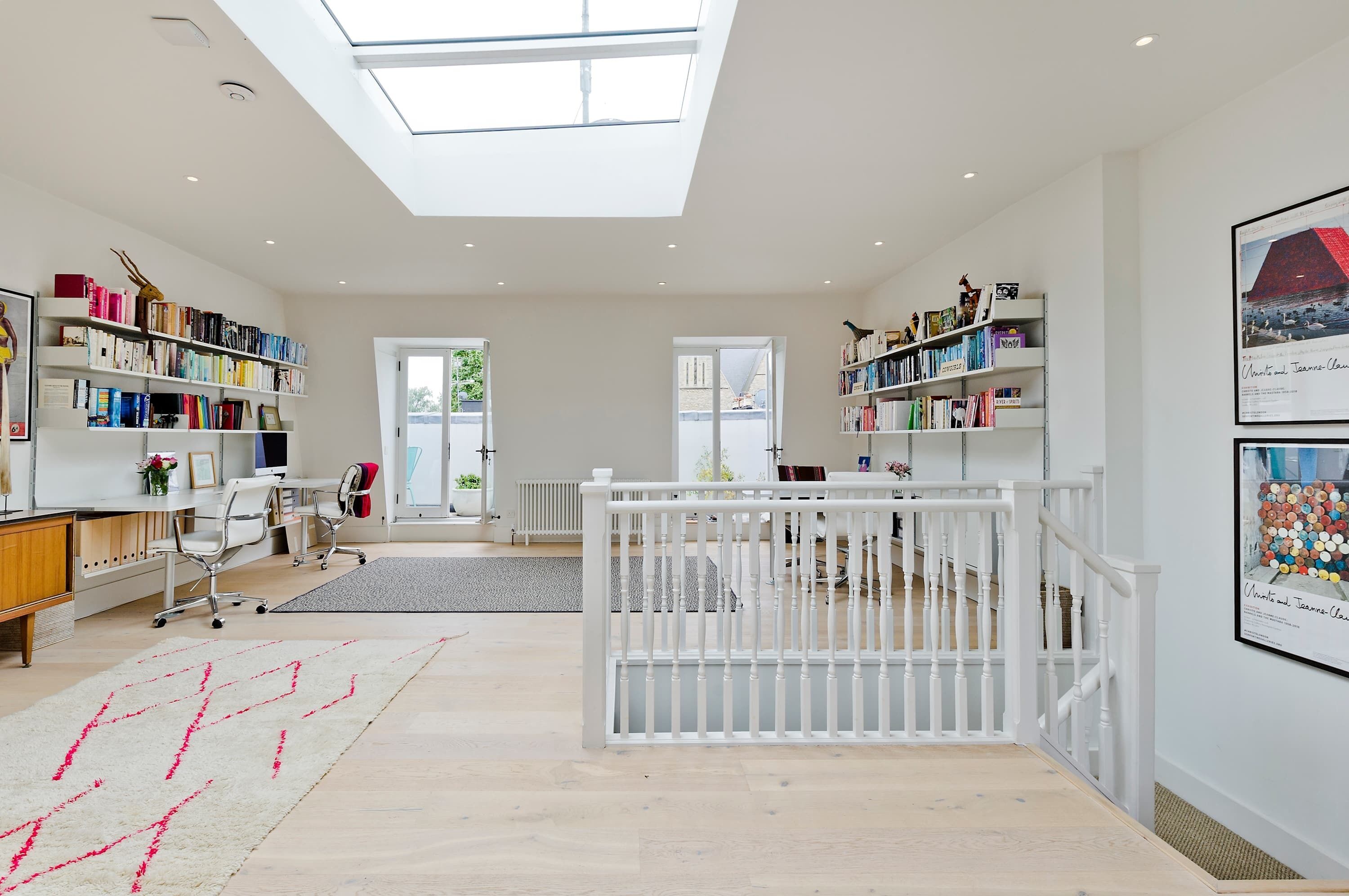 A spacious room with a skylight, a white railing, and bookshelves filled with books.