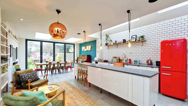 A modern kitchen with a central island, a red refrigerator, and a dining area with a view of the garden. - 4 Bedroom House, Barnes (London)