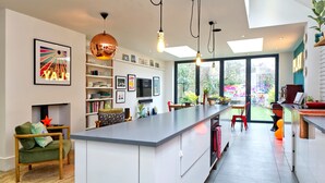 A modern kitchen with a central island, open shelving, and a view to the outdoors. - 4 Bedroom House, Barnes (London)
