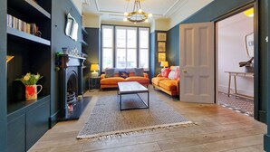A living room with a fireplace, a sofa, a coffee table, and a bookshelf. - 4 Bedroom House, Barnes (London)