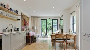 A modern kitchen with white cabinets, a dining area with wooden chairs, and a large window with a view of greenery.