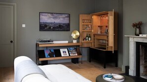 En moderne stue med en sofa, et træskab med glasvarer, en pejs og et bybillede på væggen.
