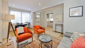 Una sala de estar moderna con un sofá gris, sillones naranja, una mesita redonda y una lámpara.