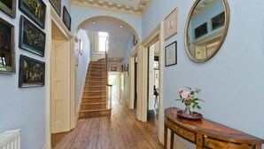 A hallway with wooden flooring, a staircase, and a wooden console table with a vase of flowers. - 5 Bedroom House, Maida Vale (London)