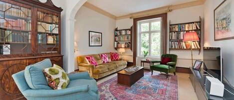 Una sala de estar con un sofá, un sillón, una mesa de centro y una amplia estantería de madera.