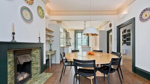 A dining area with a round wooden table, black chairs, a fireplace, and decorative plates on the walls. - 5 Bedroom House, Maida Vale (London)
