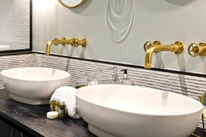 A bathroom with two white sinks, gold faucets, and a large mirror.