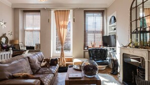 A living room with a leather sofa, a wooden coffee table, a glass bowl, a fireplace, and a television. - Stylish 1-bed With a Roof Terrace (London)