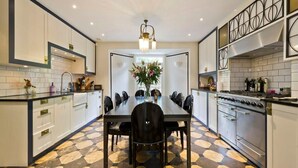 A modern kitchen with a dining area, featuring a large table, chairs, and a central vase with flowers. - Stylish 5 Bed House in St. John's Wood/maida Vale (London)
